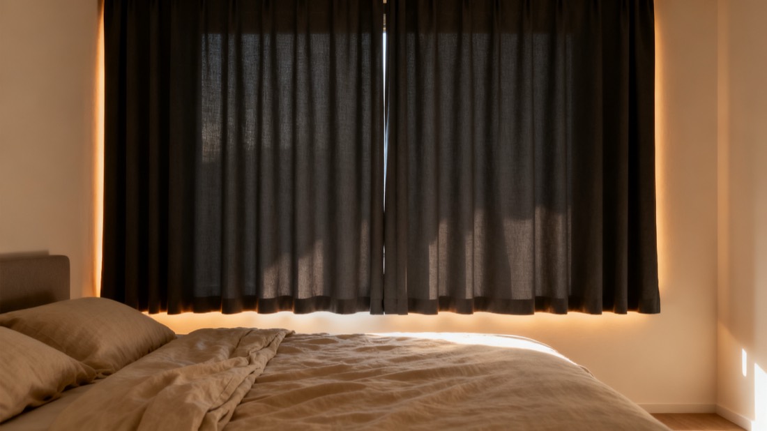 Bedroom kept dim at midday by fully closed charcoal blackout curtains
